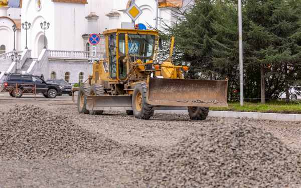 Road grader spreading crushed stone on a road under construction — stock photo